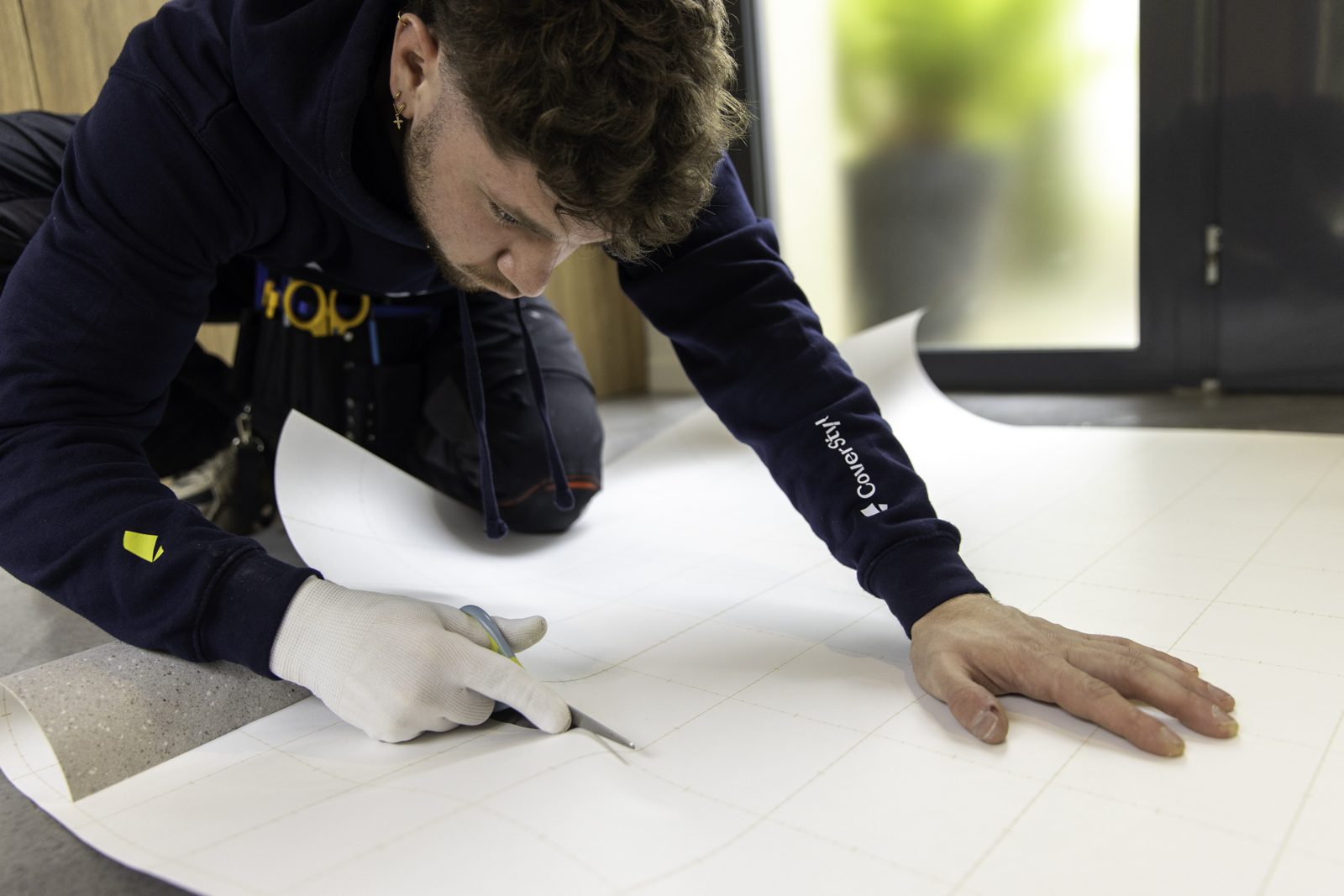 Instalador cortando una tira de vinil sobre el piso, siguiendo la cuadrícula del papel